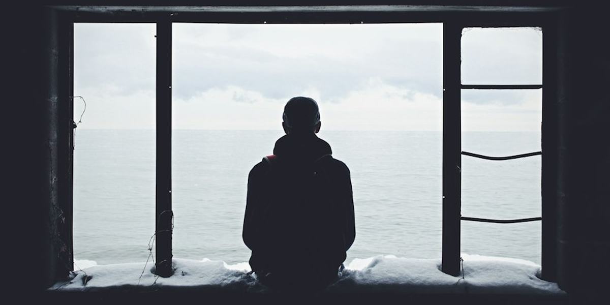 A person sitting alone at a window, looking out at the sea