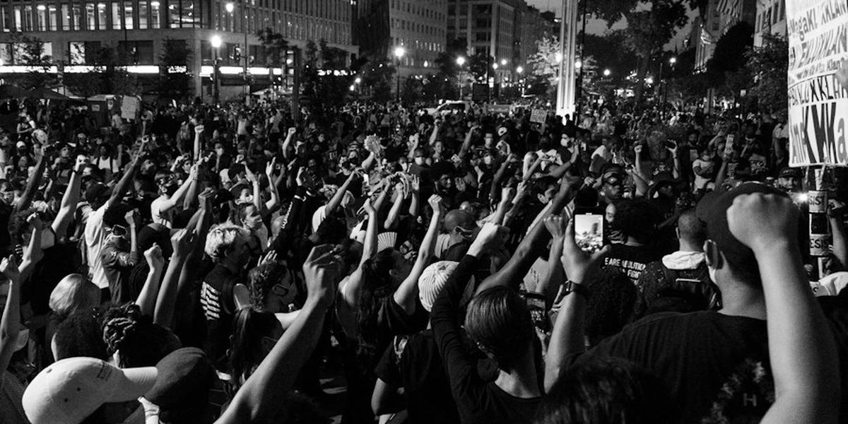 A crowd with raised arms at a night rally, in black and white
